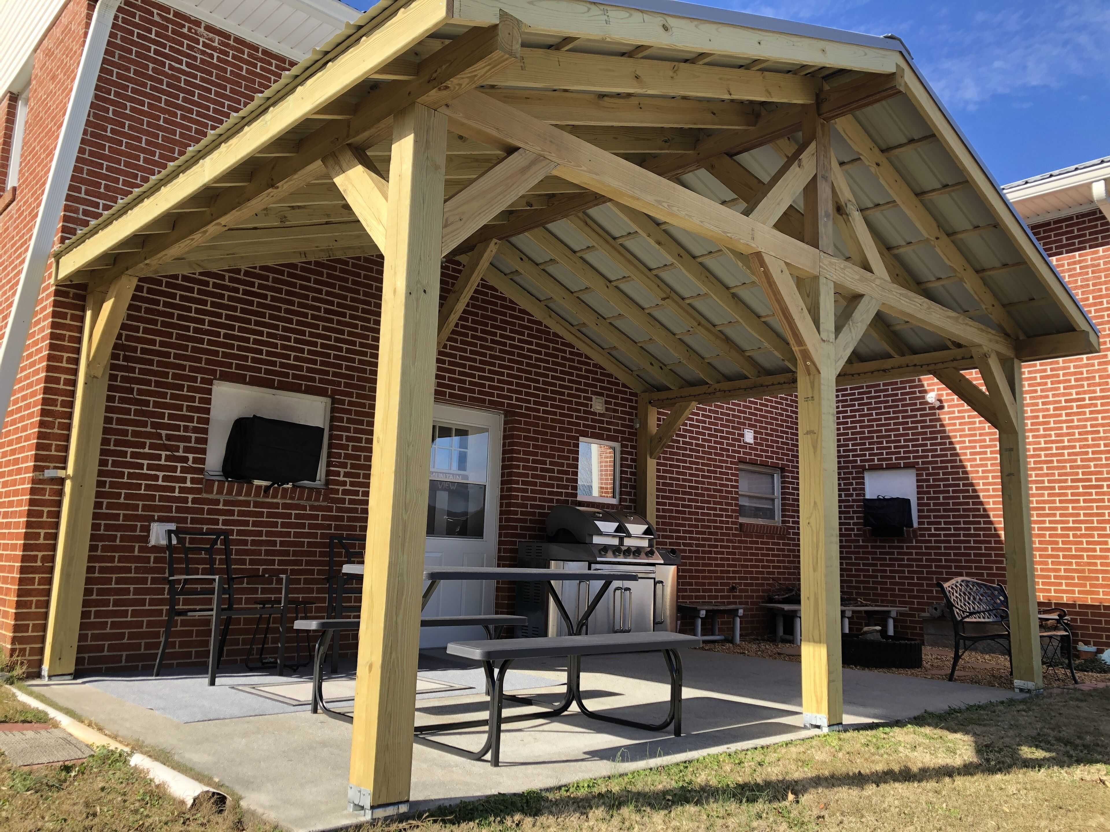 Une terrasse extérieure couverte, avec un bâtiment en briques, des tables de pique-nique et un barbecue.
