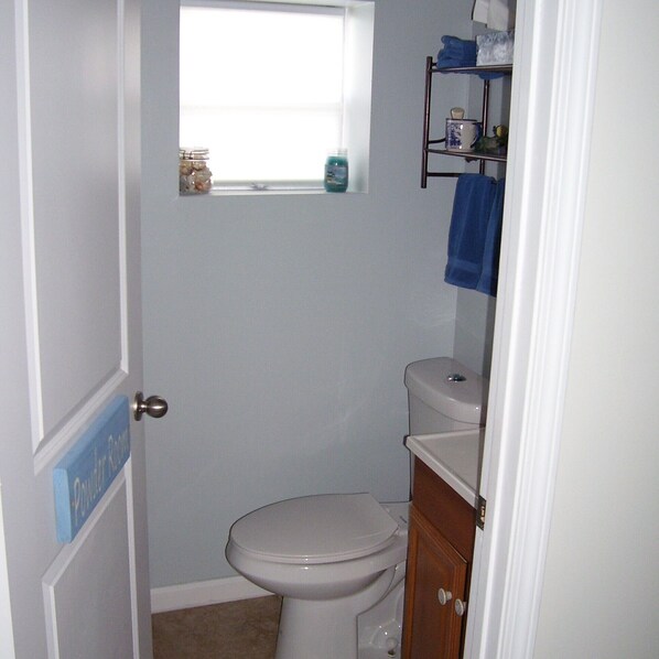 A small bathroom with a toilet, a window, and a shelf with toiletries.