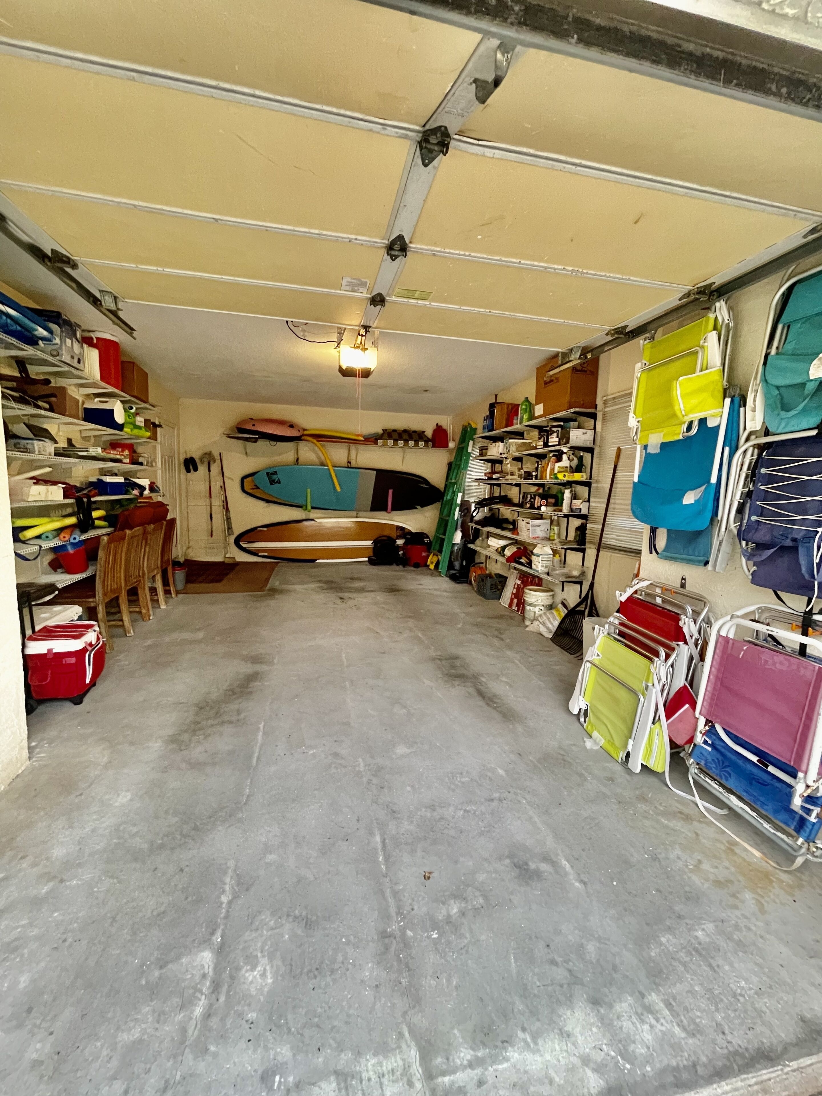 A garage with various items stored on shelves and hanging, including surfboards, a ladder, and cleaning supplies.