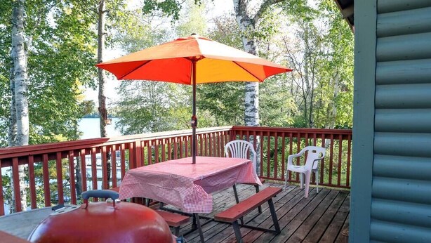 A wooden deck with a table and chairs, a barbecue grill, and a red umbrella. - Lakeview cabin on stunning Lake Vermilion (Tower)