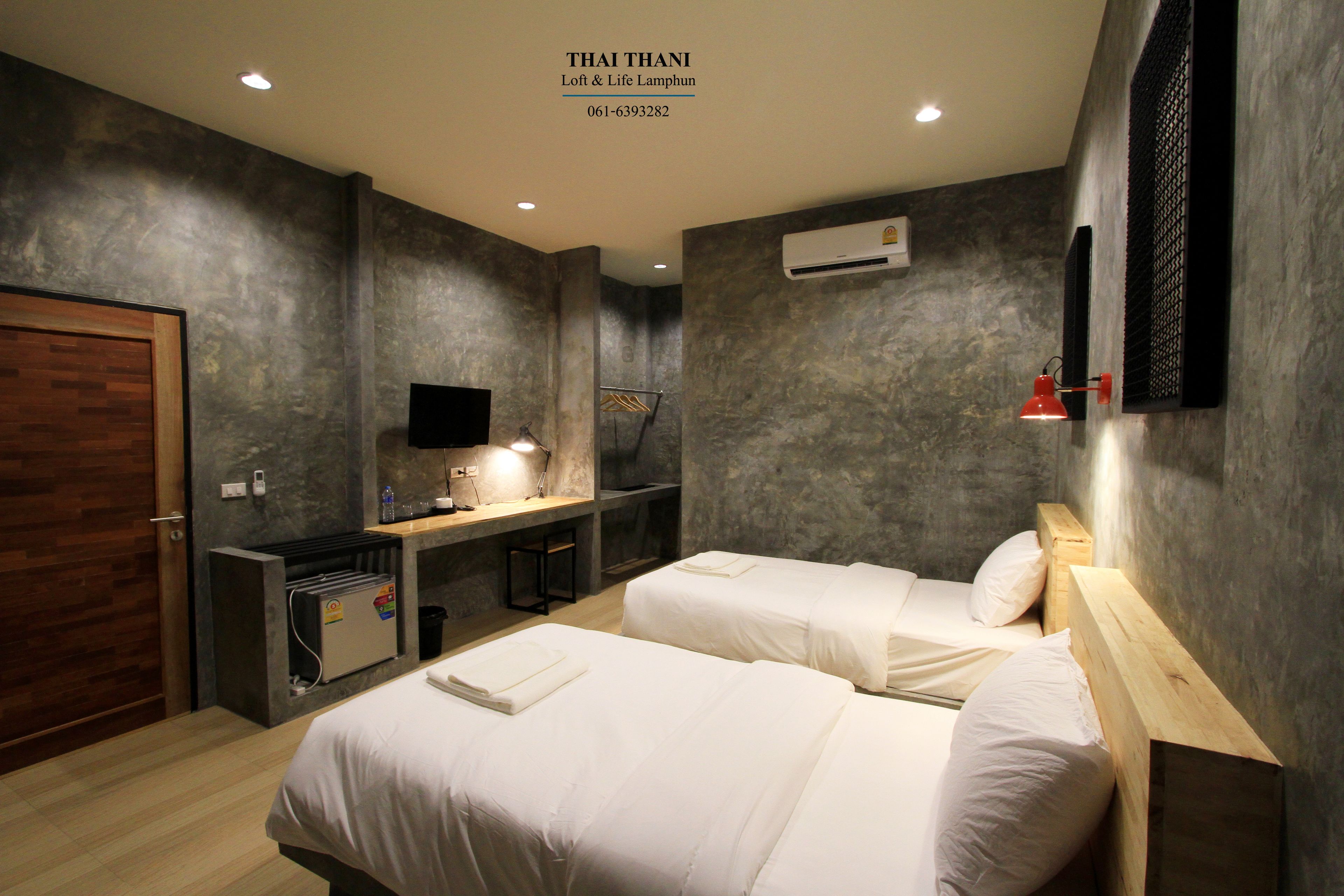 A modern hotel room with two beds, a desk with a chair, a TV, and a small kitchenette.