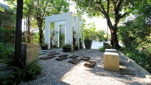 A garden with a white archway, gravel paths, and potted plants. - Thai Thani Loft & Life Lamphun (Lamphun)