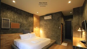 A modern bedroom with a wooden headboard, a large bed, an air conditioning unit, and a desk with a lamp. - Thai Thani Loft & Life Lamphun (Lamphun)