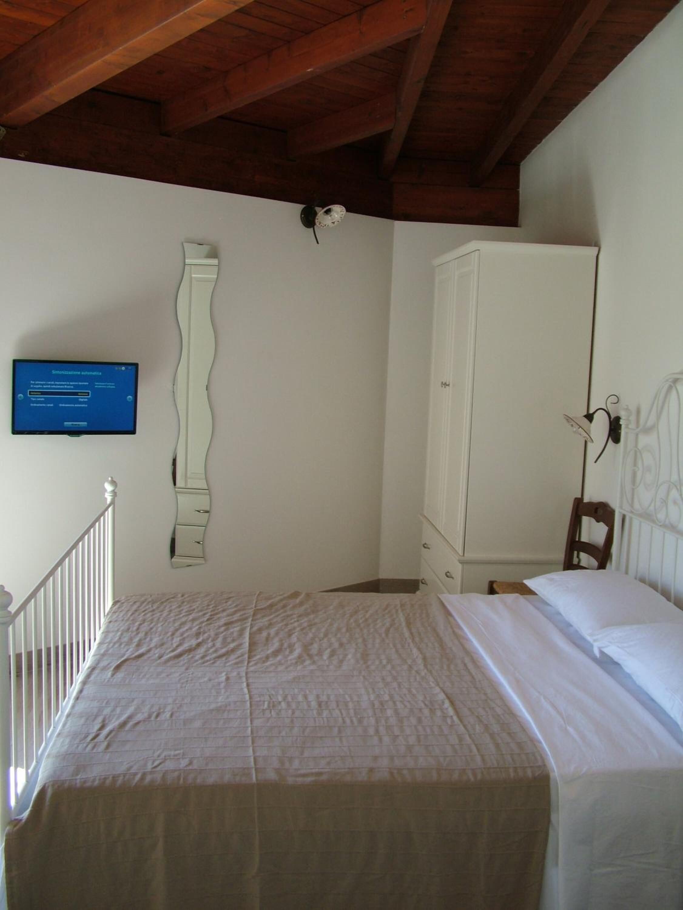 Une chambre à coucher avec un lit, une armoire, un miroir et un téléviseur fixé au mur.