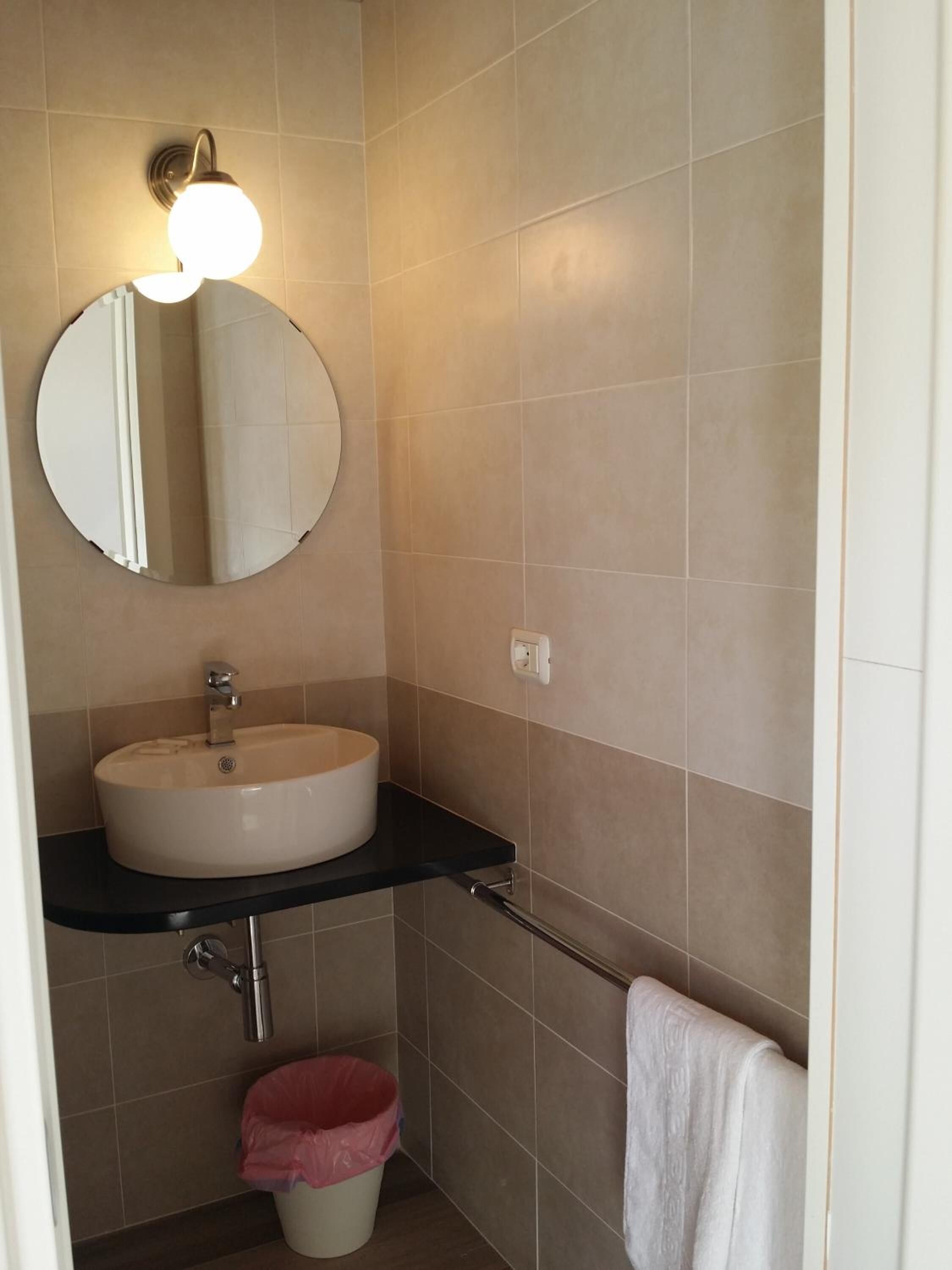 Een badkamer met een ronde spiegel, een wastafel en een handdoekhouder.