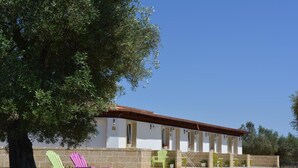 Un bâtiment à l’extérieur blanc et au toit rouge, entouré de verdure et doté d’un espace extérieur aménagé pour s’asseoir.