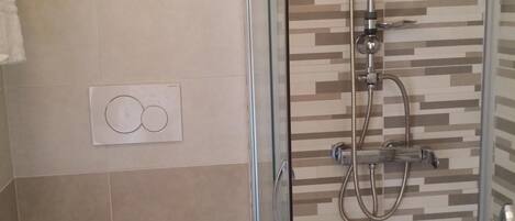 Um chuveiro com porta de vidro, parede revestida com padrão geométrico e vaso sanitário com tampa branca.