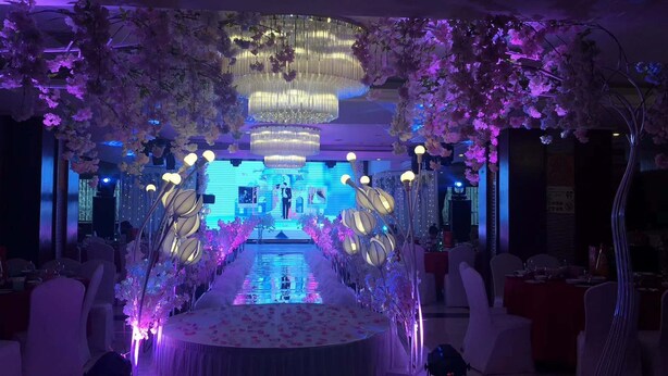 Un espacio para eventos formales con un escenario central, decoración floral e iluminación ambiental.