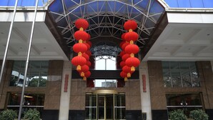 Entrada de un edificio con puerta giratoria de vidrio, faroles rojos y plantas en macetas.