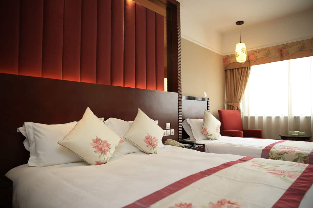 Una habitación de hotel con dos camas, una silla roja, una mesita de noche y una ventana con cortinas.