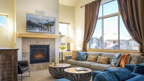 Una sala de estar con chimenea, un conjunto de sofá y un ventanal con cortinas.
