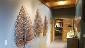 Un pasillo con tres grandes esculturas de hojas montadas en la pared, un escritorio de madera con una lámpara, y una puerta que conduce a una habitación con una cama y un escritorio.
