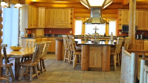 Cocina estilo cabaña de troncos con armarios de madera, una isla central con taburetes y una lámpara colgante grande.