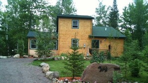 A log cabin with a gravel driveway, surrounded by a garden with rocks and small trees. - Bearadise On the Thornapple River (Ladysmith)