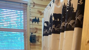 A room with wooden panel walls, a window with blinds, a scale on the floor, and a curtain with a forest pattern. - Bearadise On the Thornapple River (Ladysmith)