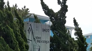 Un panneau en bois portant le numéro 1437 et le nom « The Riggings », placé dans un espace aménagé avec du paillis, des plantes et une clôture en bois.