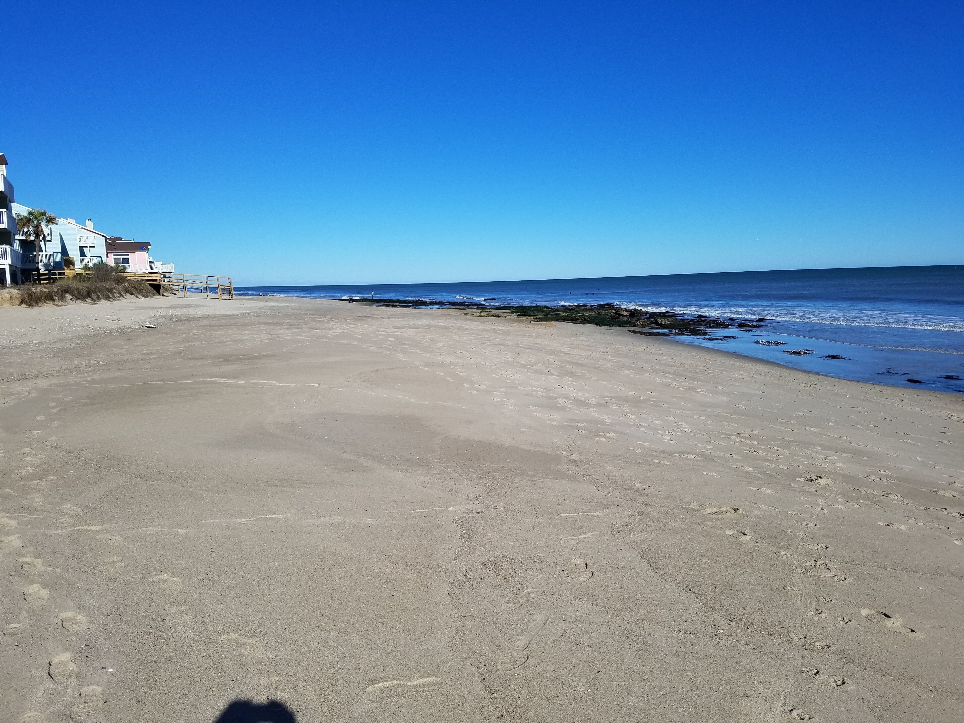 Una extensa playa de arena con cielo azul despejado y mar tranquilo.