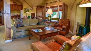 Una sala de estar acogedora con un sofá, sillones y una mesita de centro. Hay una chimenea, una lámpara y una ventana con cortinas.