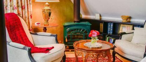 A cozy living room with a fireplace, a red throw blanket on a chair, a lamp, and a bookshelf.