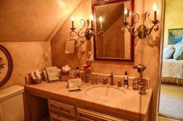 Un baño con un lavamanos grande, tocador y espejo. Hay velas en la pared y un florero sobre el mostrador.