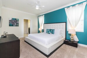 Une chambre avec un lit blanc, des murs de couleur turquoise, un ventilateur de plafond et une table de chevet avec une lampe.