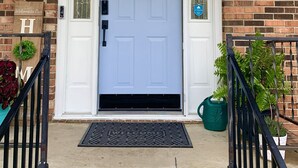 A front door with a blue door, a white doorbell, a welcome mat, and a brick wall.