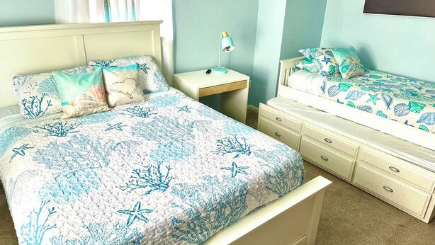A bedroom with a bed, a nightstand, a dresser, and a wall-mounted lamp.