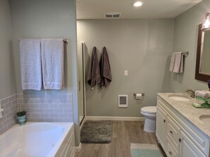 Enjoy a refreshing bath in the spacious bathroom with a large bathtub, walk-in shower, and vanity with sink and mirror.