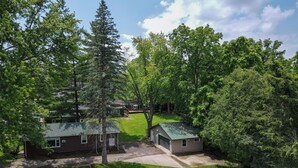 A cabin with a green roof, surrounded by dense trees and a well-maintained lawn. - Two Bed Two Bathroom Cabin with kitchenette area (Williams Bay)
