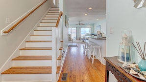 A staircase with wooden steps and white walls, leading to a kitchen area with a bar and a view of the outdoors. - 🌊Mission SEA Accomplished🌊 Ocean Views, Private Grill, Steps 2 Beach (Kure Beach)