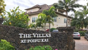 A sign for "The Villas at Poipu Kai" with a stone wall and flowering plants in front.