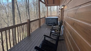 Eine Holzterrasse mit Whirlpool und Bänken, umgeben von Bäumen.