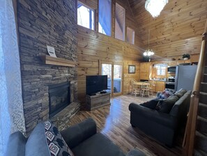 A cozy cabin interior with a stone fireplace, wooden walls, a dining area, and a kitchen. - Winter SpeciaL getaway (Sevier County)