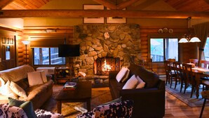 A cozy log cabin interior with a stone fireplace, wooden furniture, and a television. - Enjoy Our Beautiful Log Home  (McCloud)