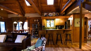 A cozy log cabin interior with a living room, a bar area, and a kitchen. - Enjoy Our Beautiful Log Home  (McCloud)