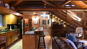 A spacious kitchen with wooden cabinets, a central island with stools, and a dining area with a sofa and chairs. - Enjoy Our Beautiful Log Home  (McCloud)
