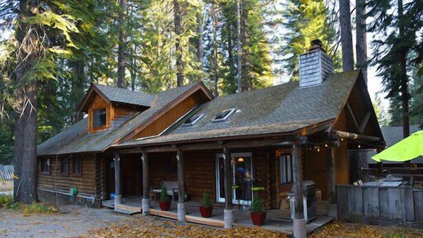 A log cabin with a porch, multiple windows, and a chimney. - Enjoy Our Beautiful Log Home  (McCloud)