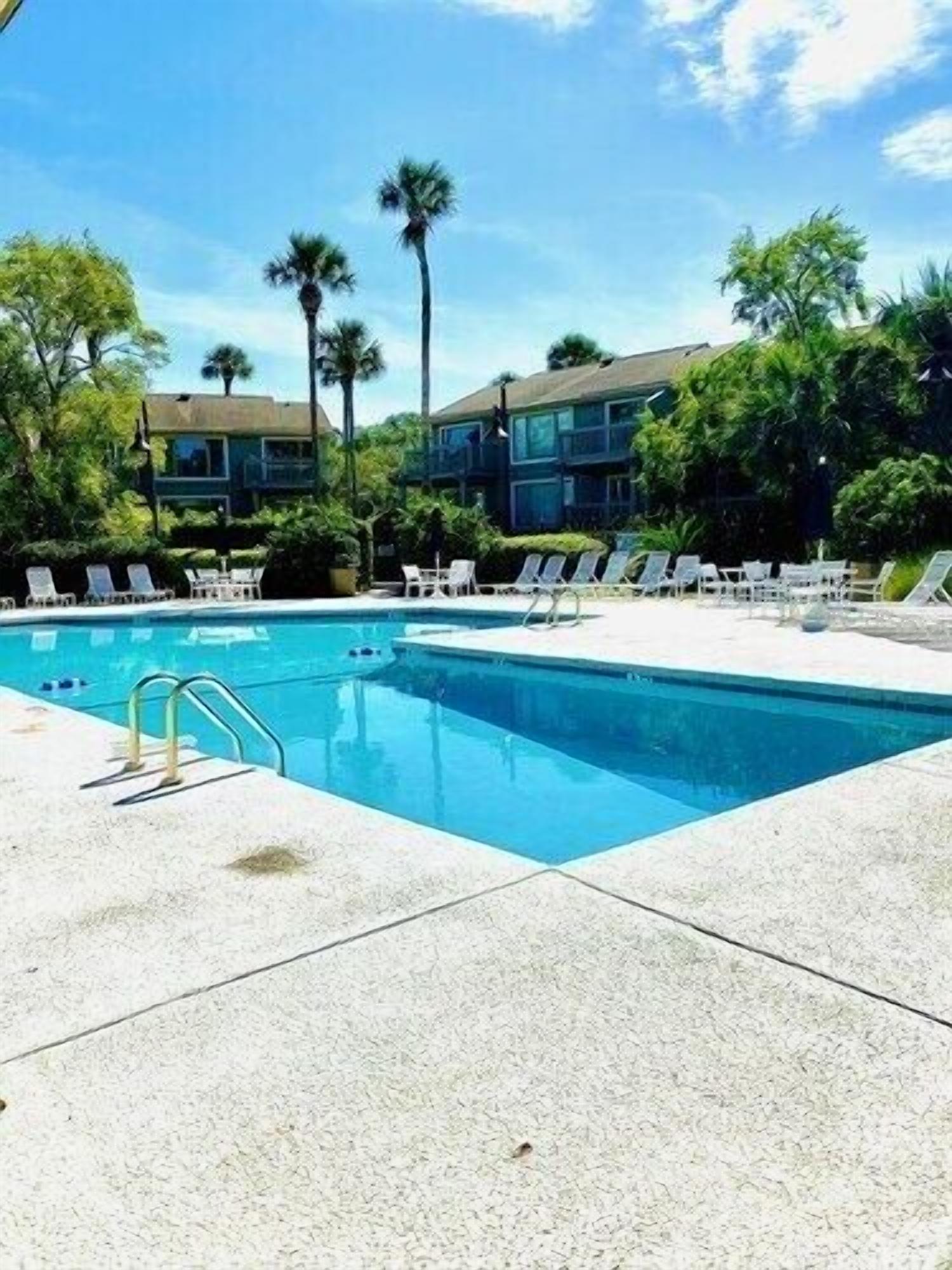 A swimming pool with lounge chairs, surrounded by palm trees and a building.