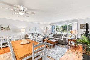 Ein geräumiges Wohnzimmer mit einem Holzespeisetisch, einem grauen Sofa und einem Deckenventilator.