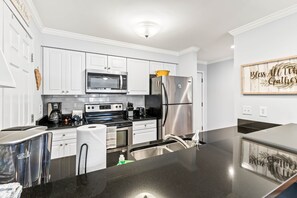 A modern kitchen with white cabinetry, stainless steel appliances, and a black countertop. - Lagoon Villa 25 - Heart of Wild Dunes! Beach/Pool! (Isle of Palms)