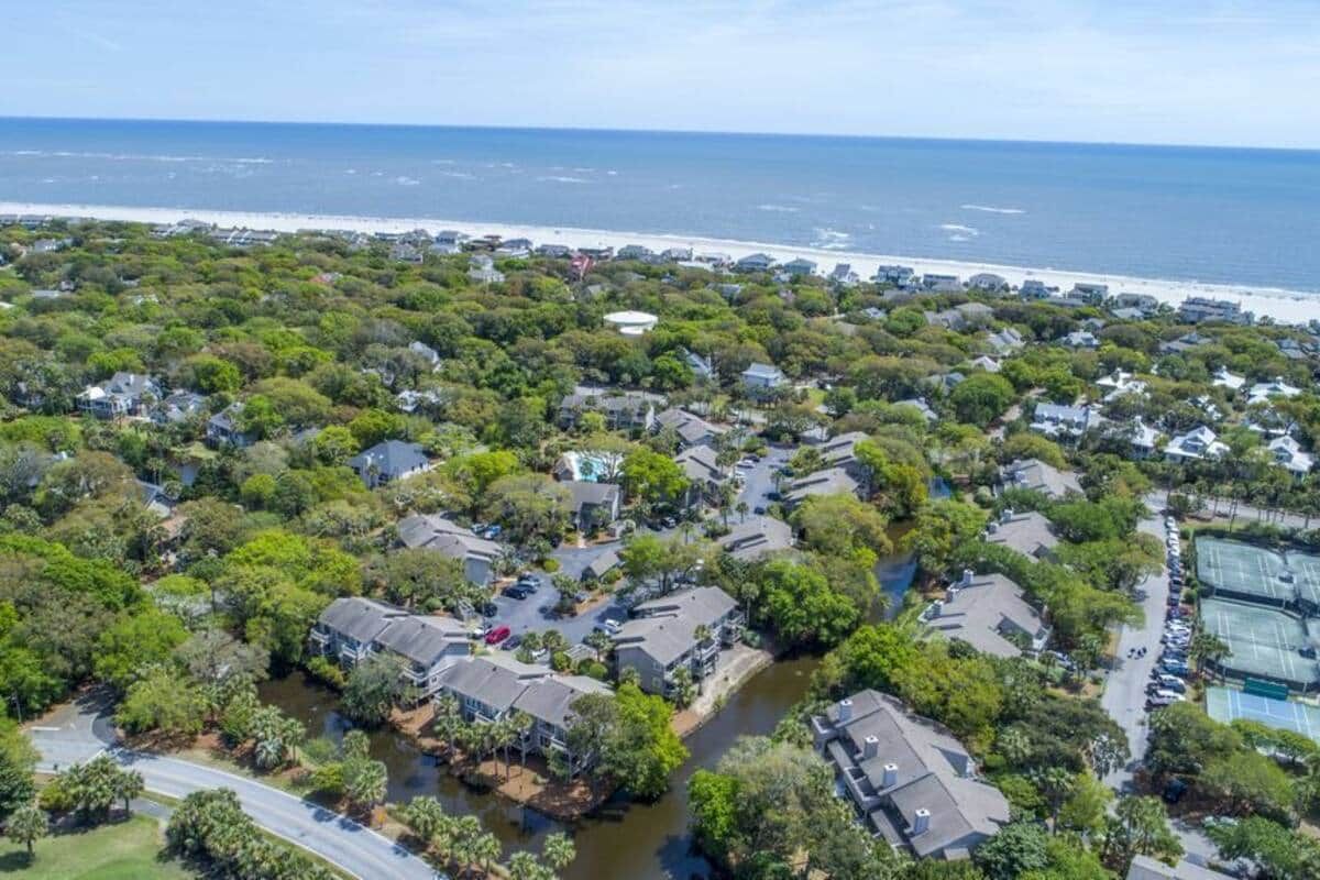 An aerial view of a residential area with houses, a river, and a beach in the background.