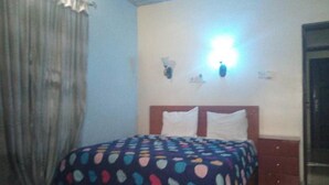 Un dormitorio con cama, cortinas, una lámpara fijada en la pared y una puerta.