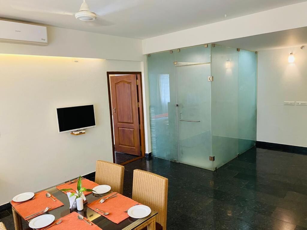Un coin repas avec une table dressée pour quatre personnes, un téléviseur fixé au mur et une porte vitrée donnant sur une autre pièce.