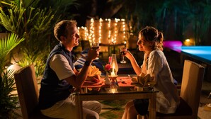 A couple dining at an outdoor table with a candle centerpiece, surrounded by lush greenery and string lights. - PepperVine (Peermade)