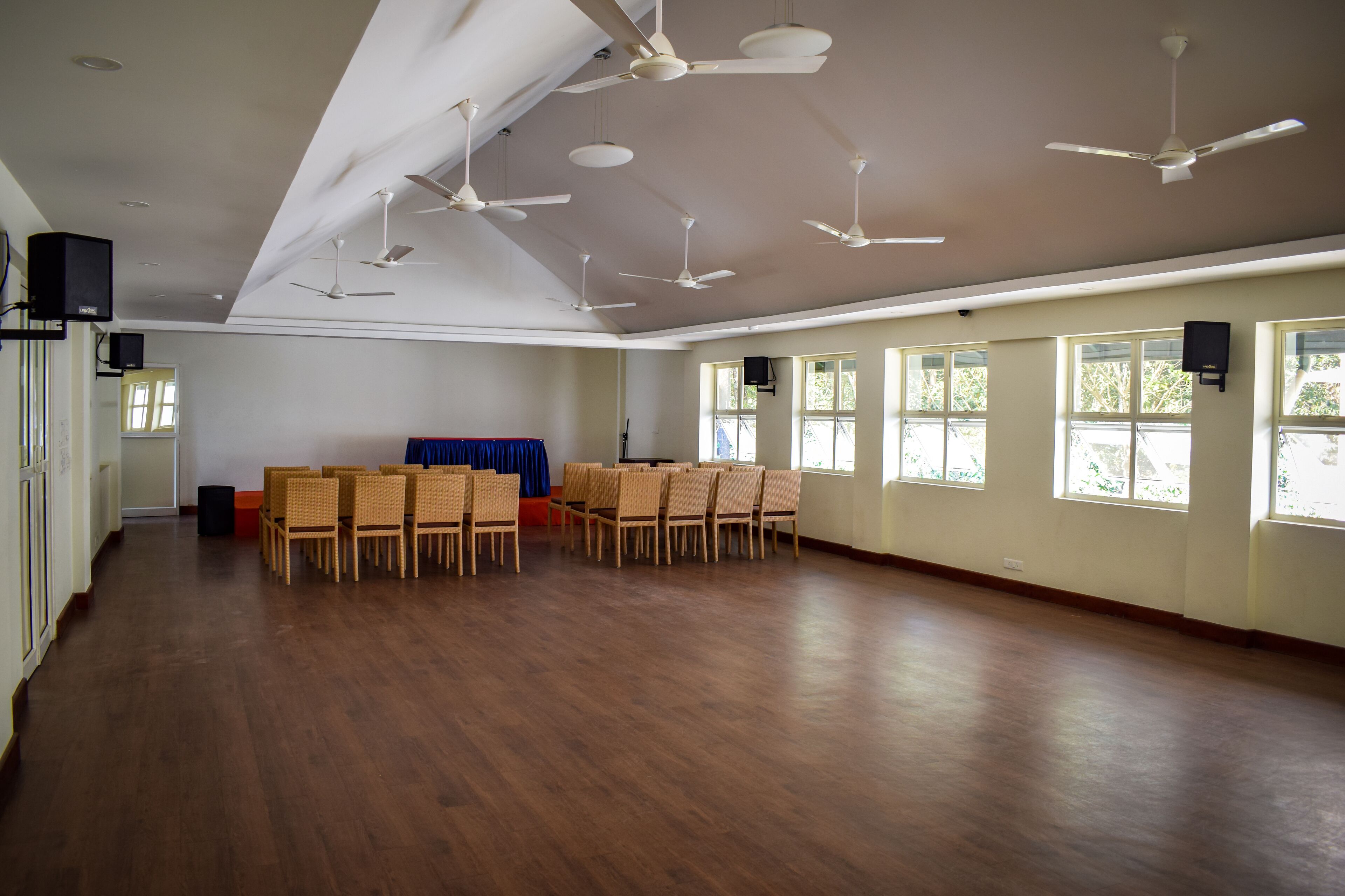 A spacious room with multiple ceiling fans, large windows, and a row of chairs.