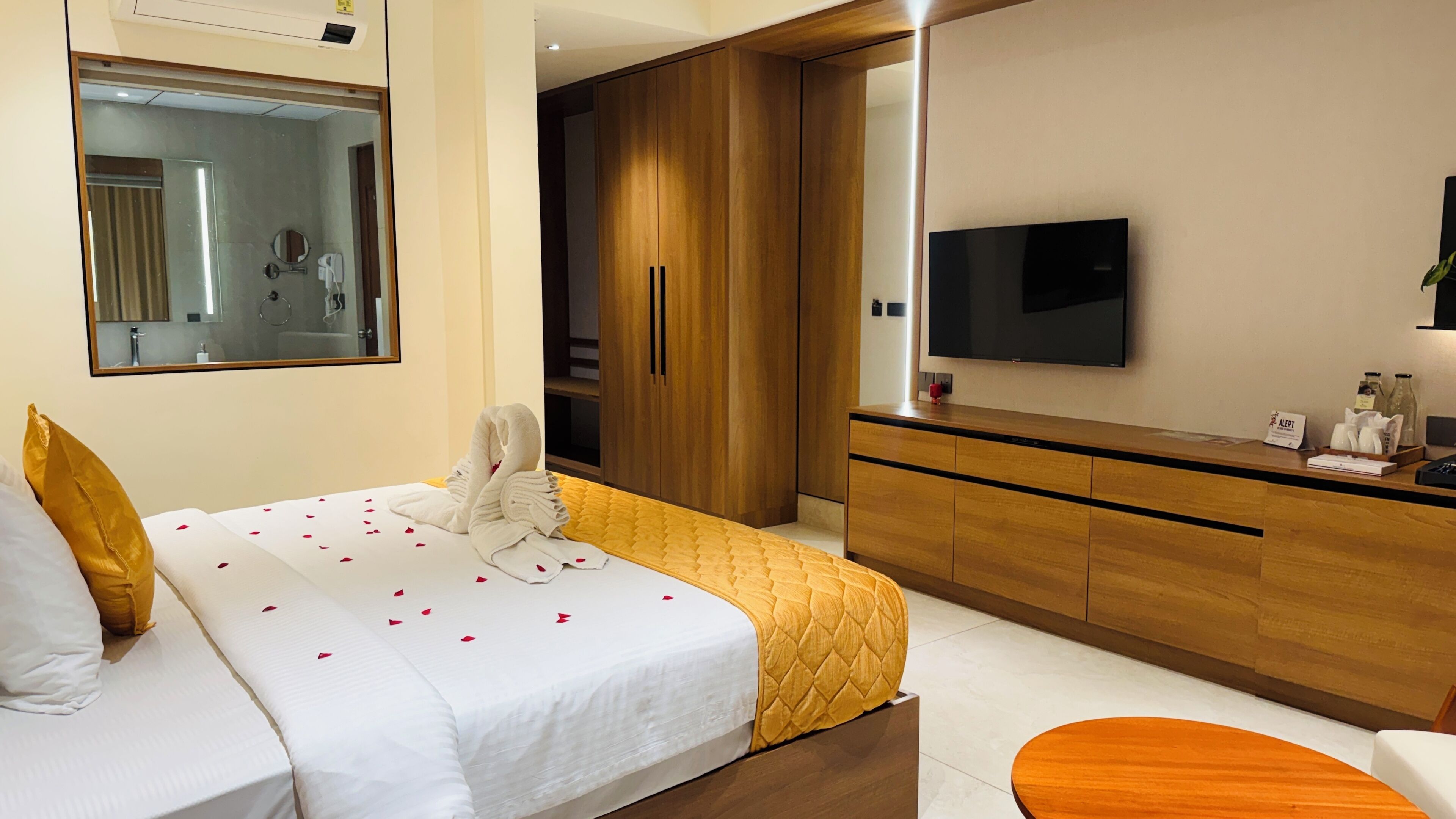 A hotel room with a bed, a wooden wardrobe, a TV, and a desk with a mirror.