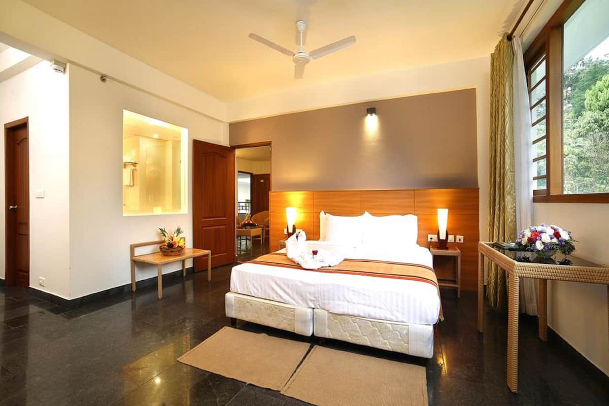 Quarto de hotel com cama, mesas de cabeceira, ventoinha no teto, janela com cortinas e vista para o exterior.
