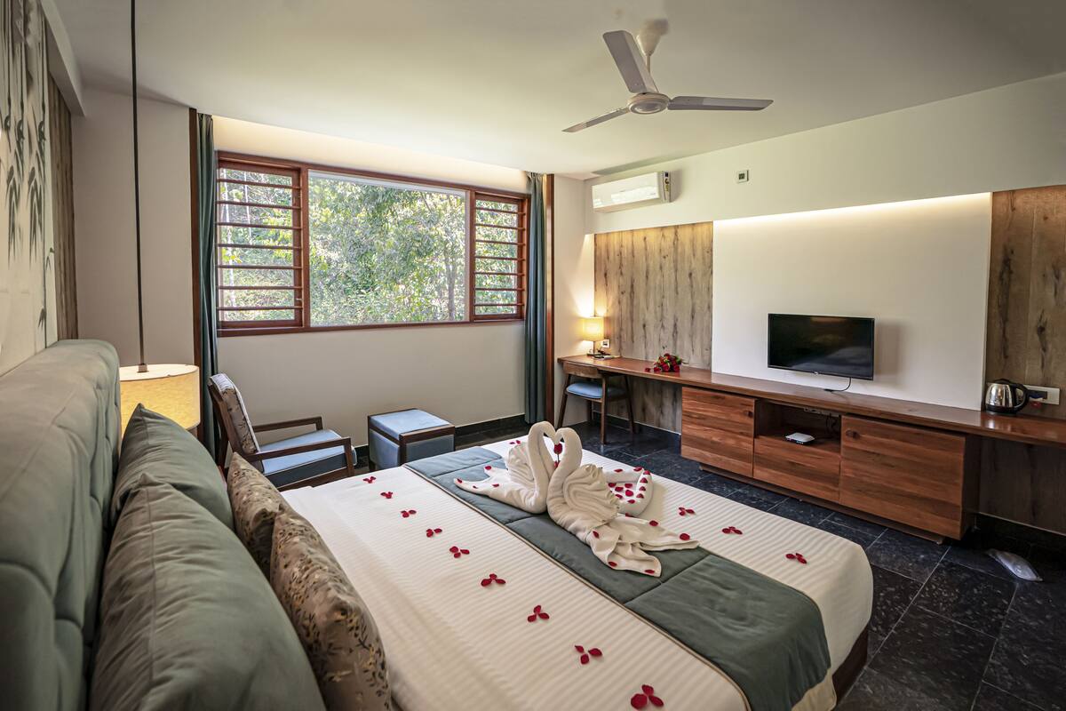 Quarto de hotel com cama, escrivaninha, televisão e ventoinha no teto.