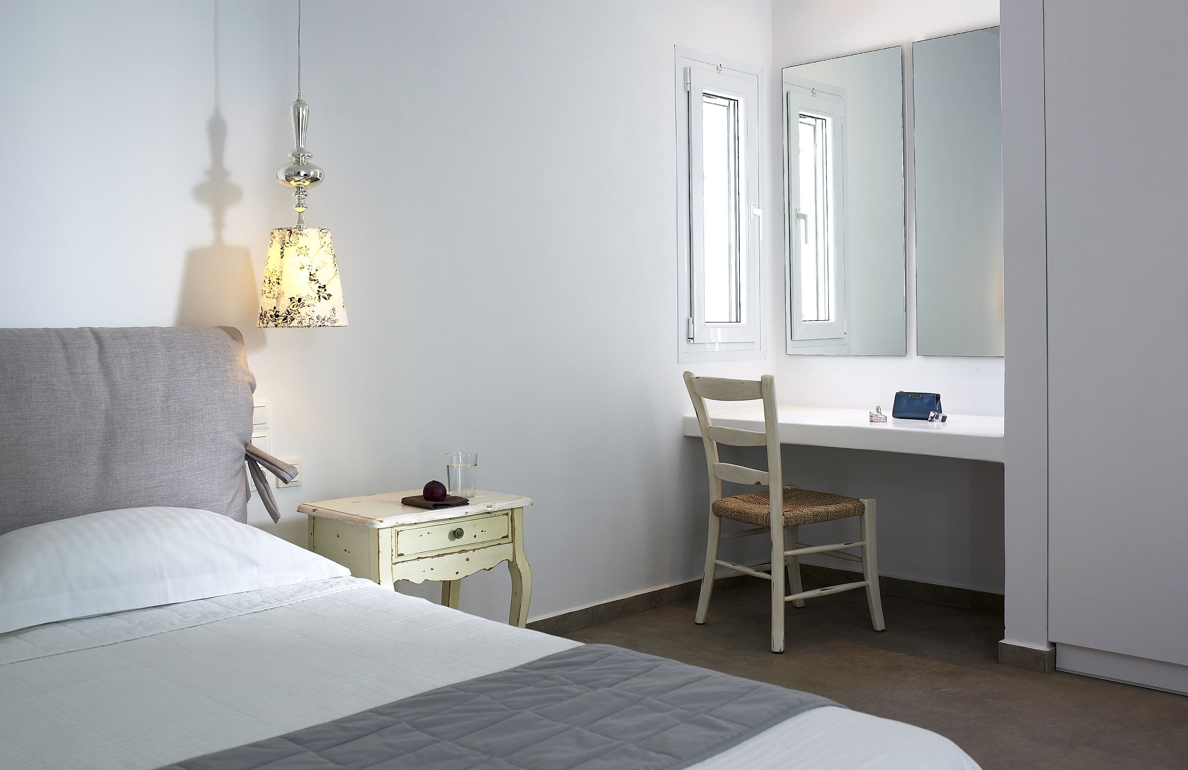 A bedroom with a bed, bedside table, chair, desk, and a mirror.