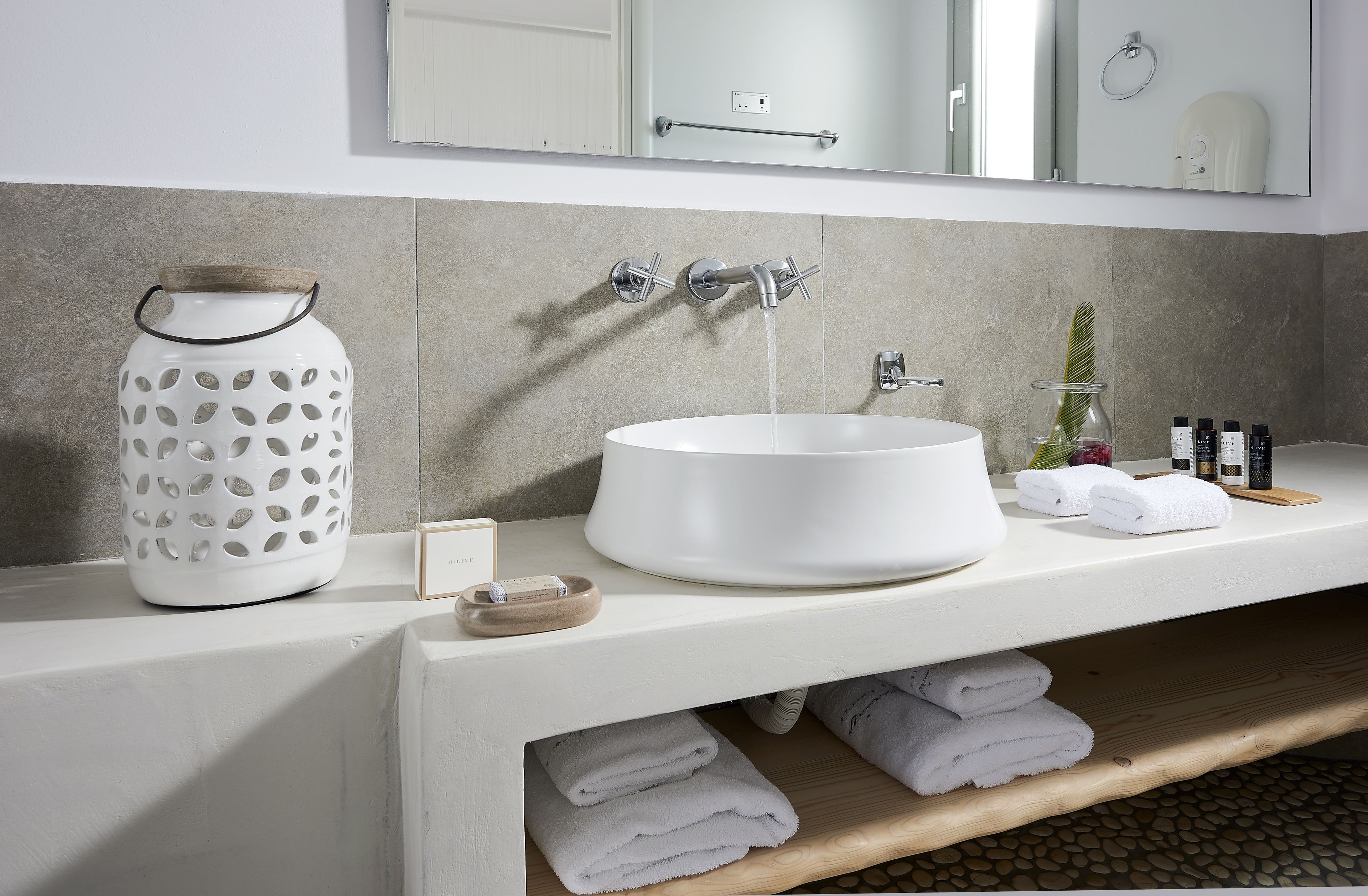 Een moderne badkamer met een witte wasbak, een grote spiegel en een houten plank met handdoeken.